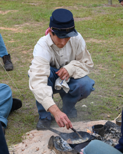 Young man squatted in front of a fire cooking food in a small pan.